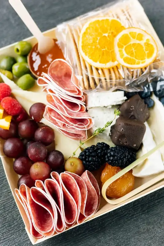 Small square board with three cheeses, cured meat, fruit and crackers (view 4)
