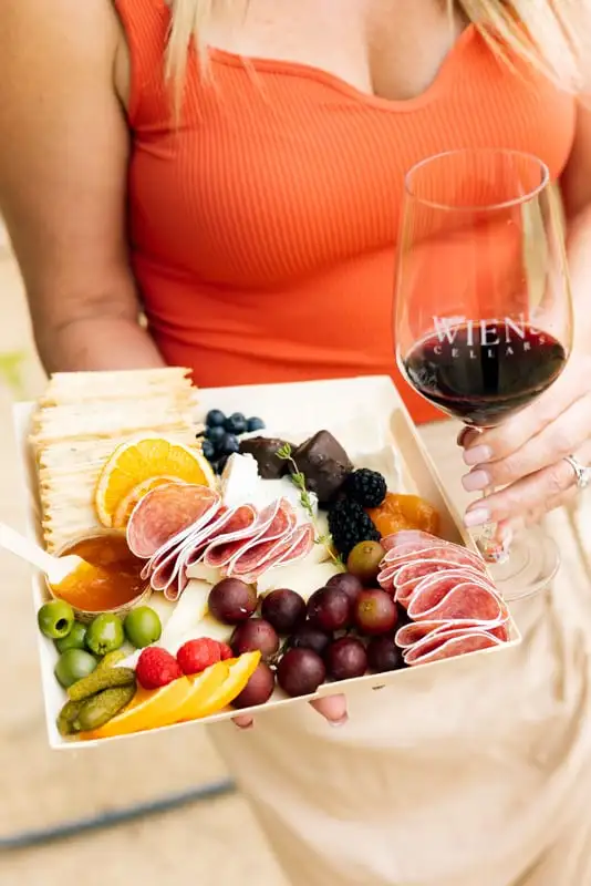 Small square board with three cheeses, cured meat, fruit and crackers