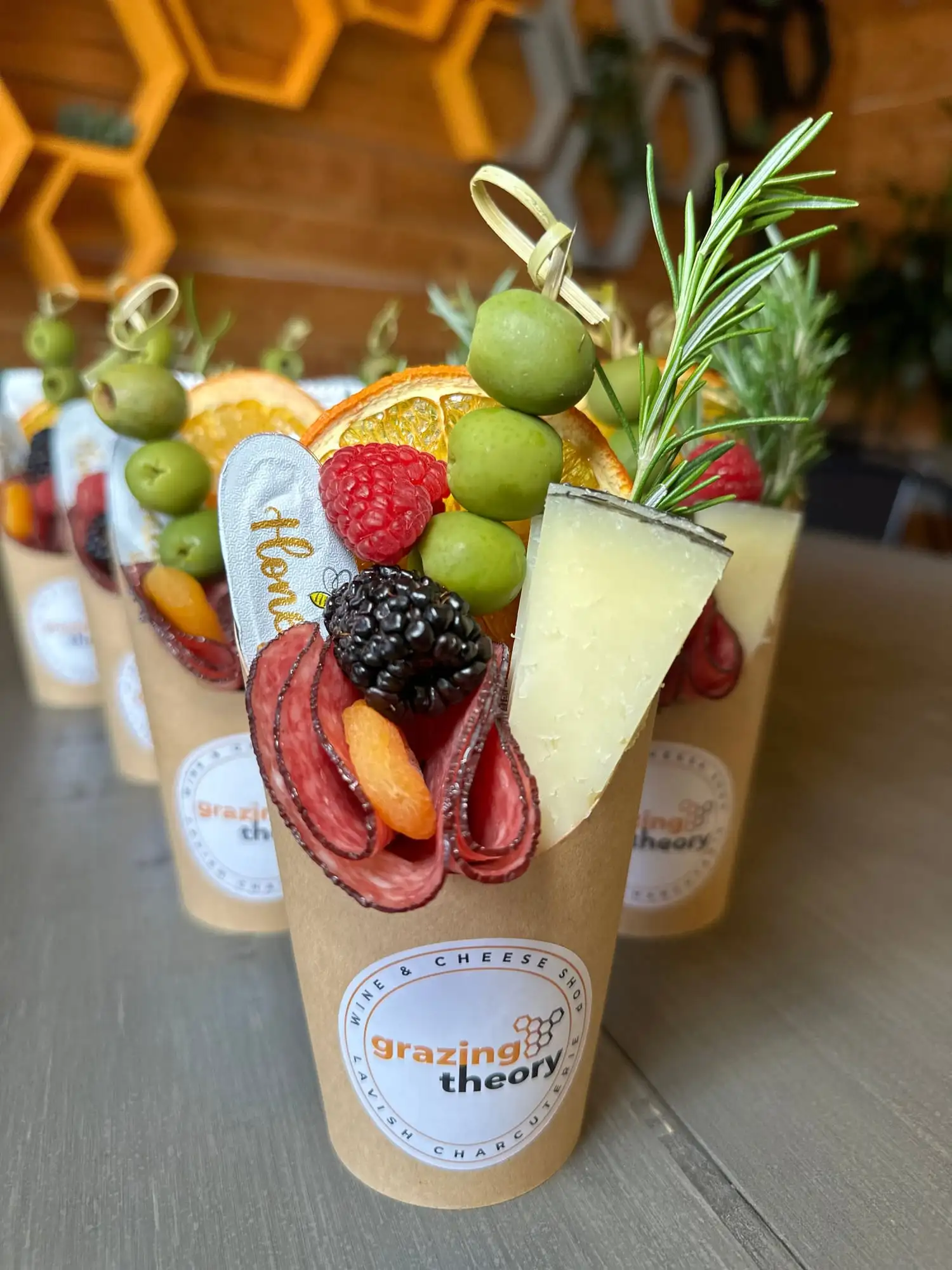 Clear cup filled with cheese, salami, olives, fruit and crackers