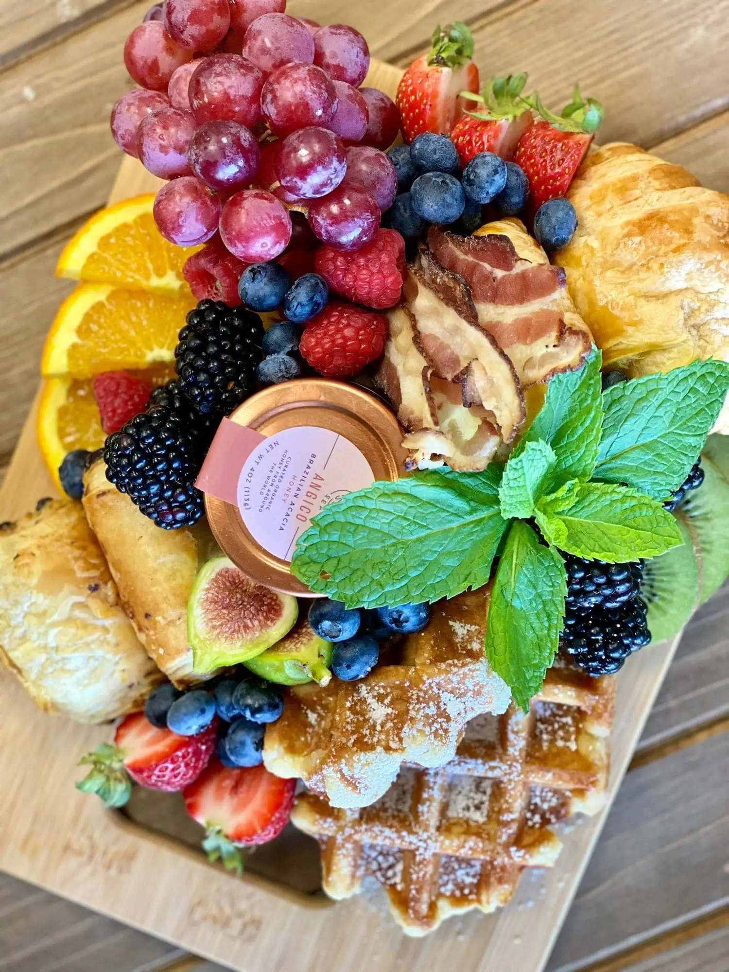 Small bamboo brunch board with croissants, waffles and fruit