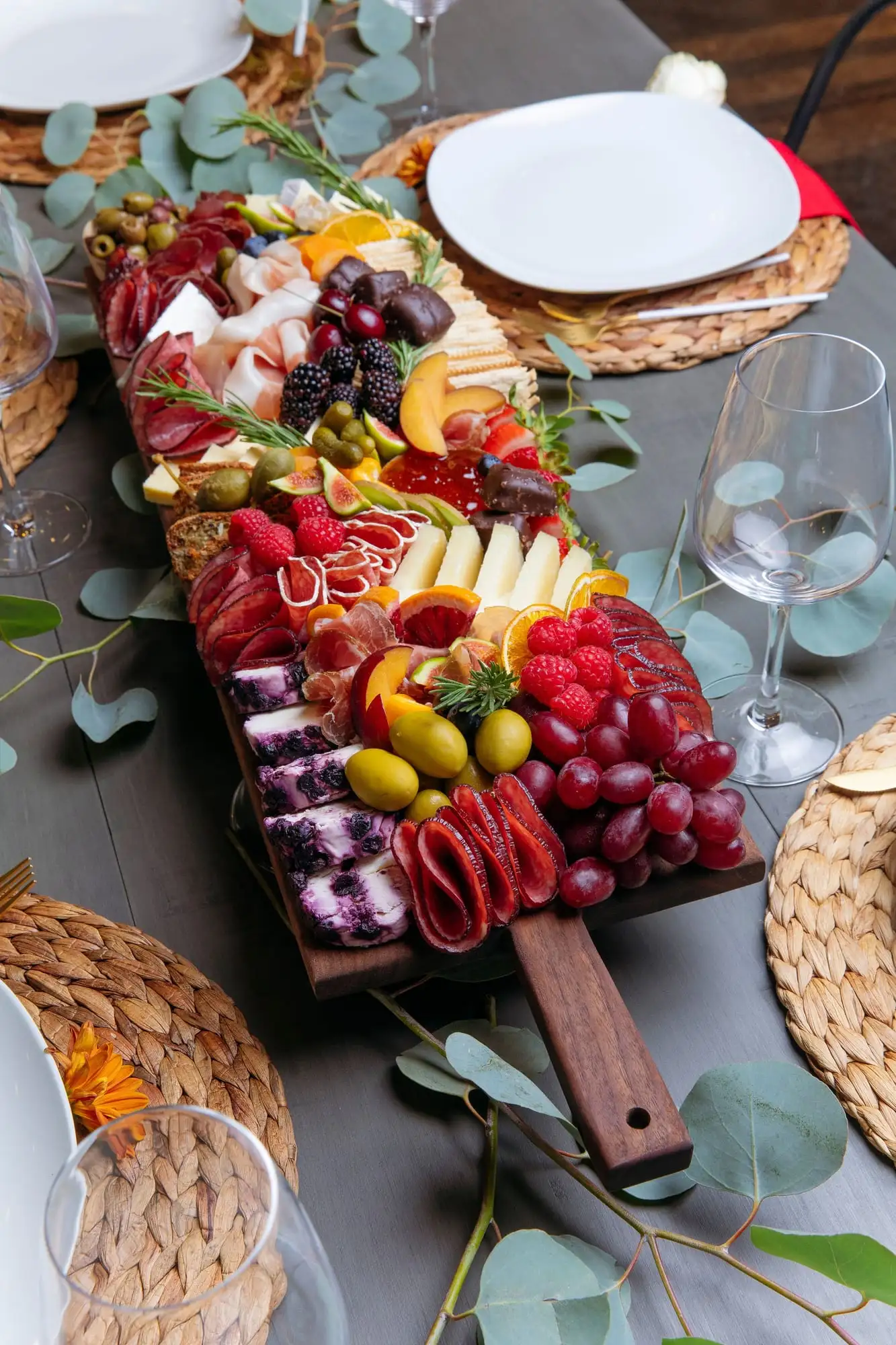 Long wooden picnic board with cheeses, charcuterie, fresh vegetables and honeycomb