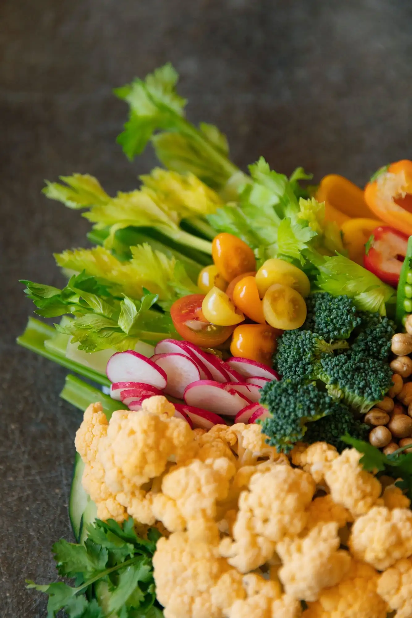 Board of rainbow carrots, peppers, snap peas and tomatoes around a bowl of hummus (view 2)
