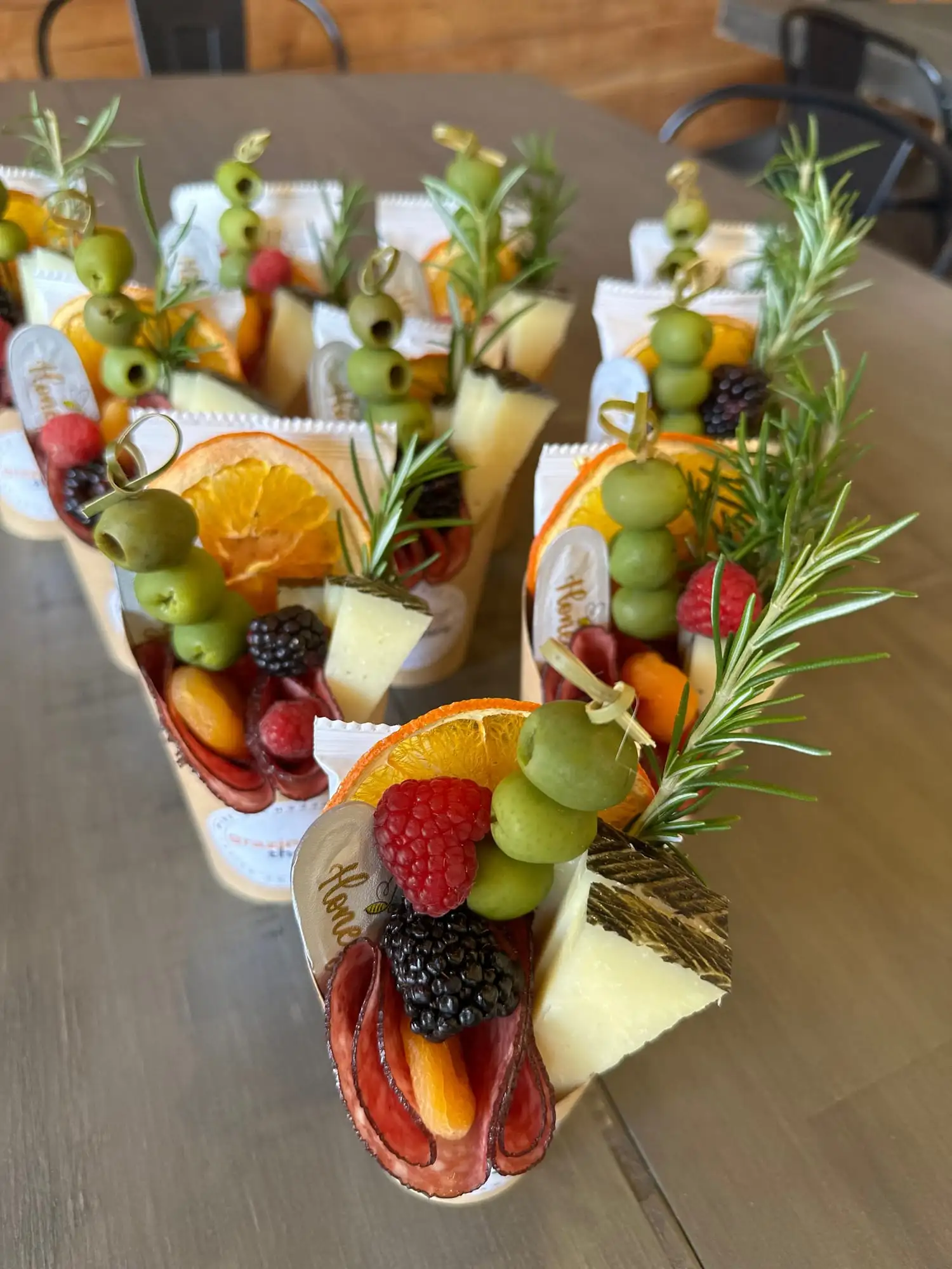 Clear cup filled with cheese, salami, olives, fruit and crackers (view 2)