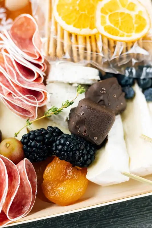 Small square board with three cheeses, cured meat, fruit and crackers (view 2)