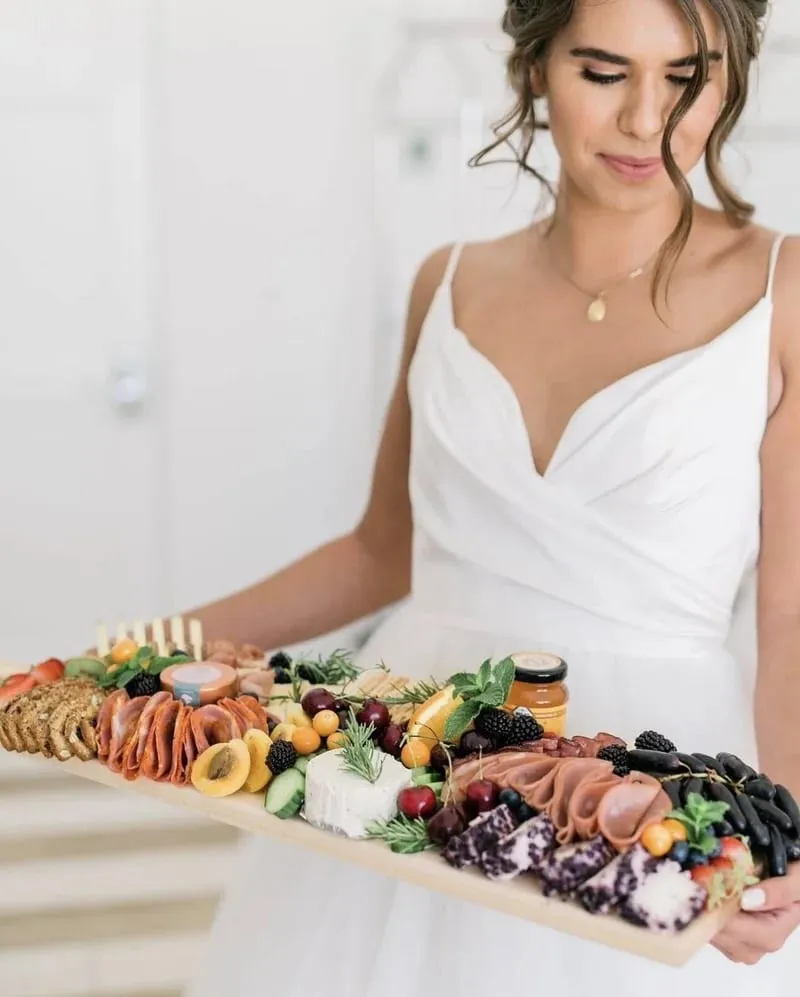 A bride in her wedding dress carrying a long charcuterie board