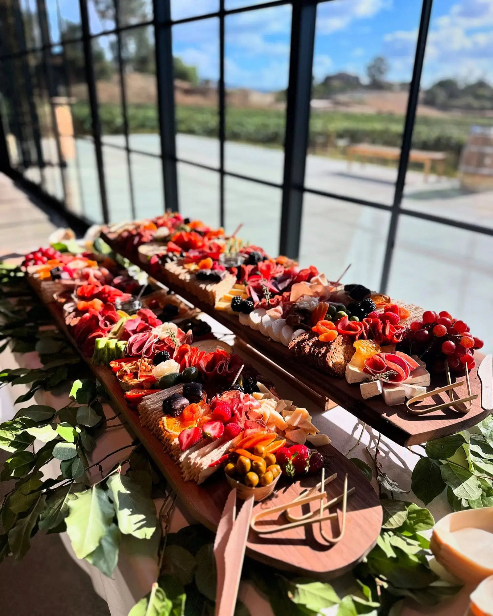 Two Boujee Boards of cheeses, cured meats and fruit on a table by tall windows