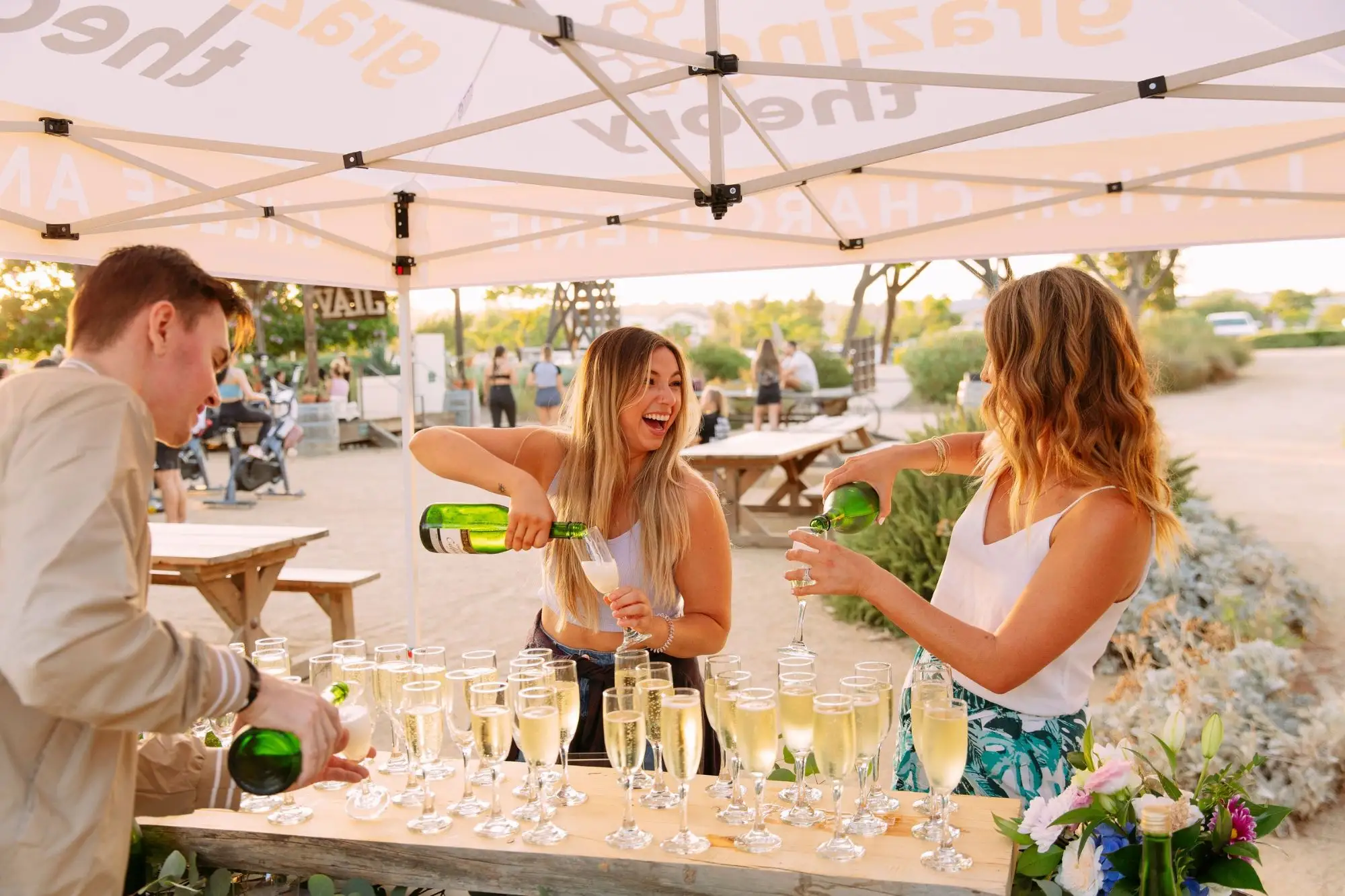 Grazing Theory team pouring champagne into rows of glasses under the Grazing Theory tent at golden hour