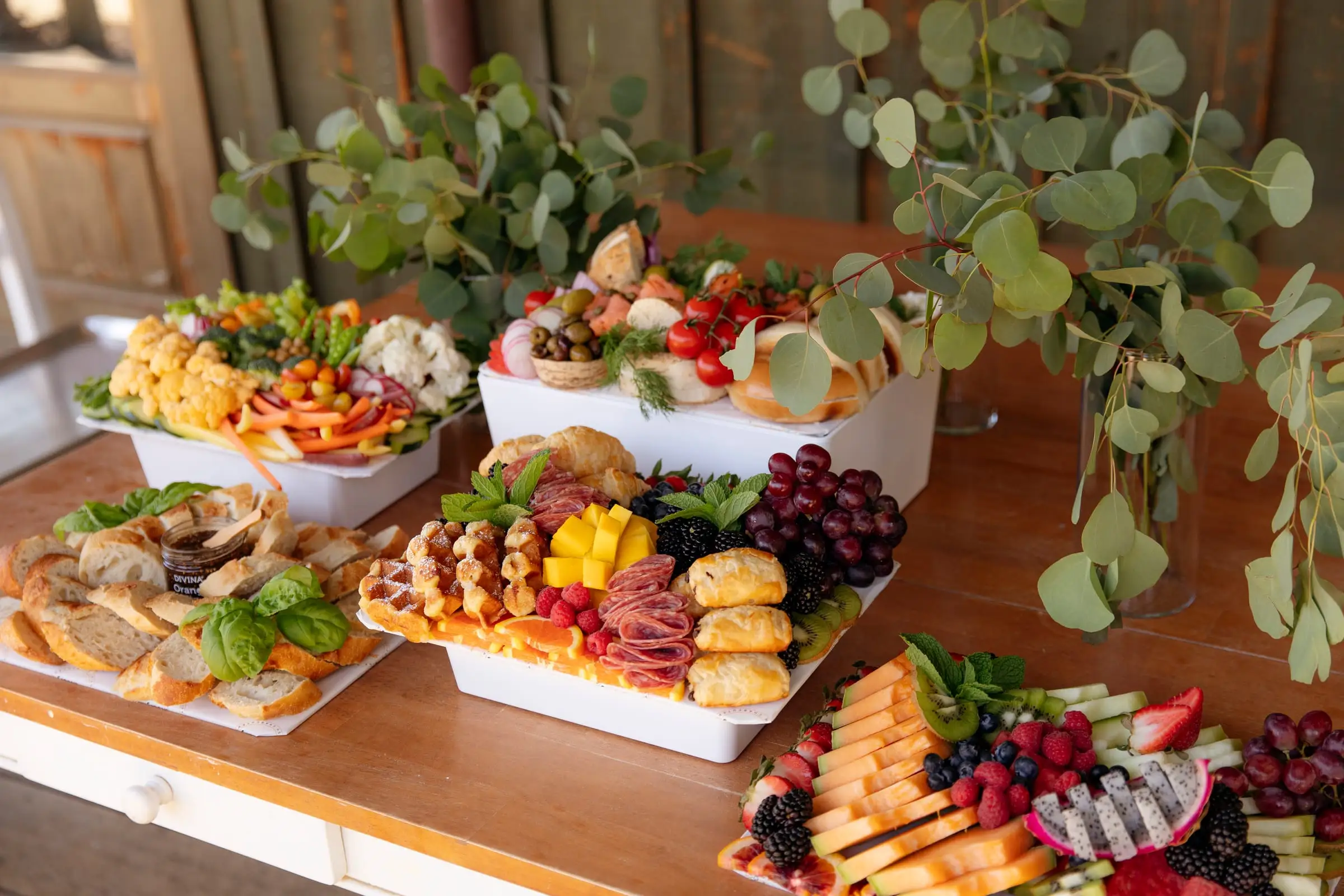 Several charcuterie, fruit and veggie boards arranged on white risers for a party