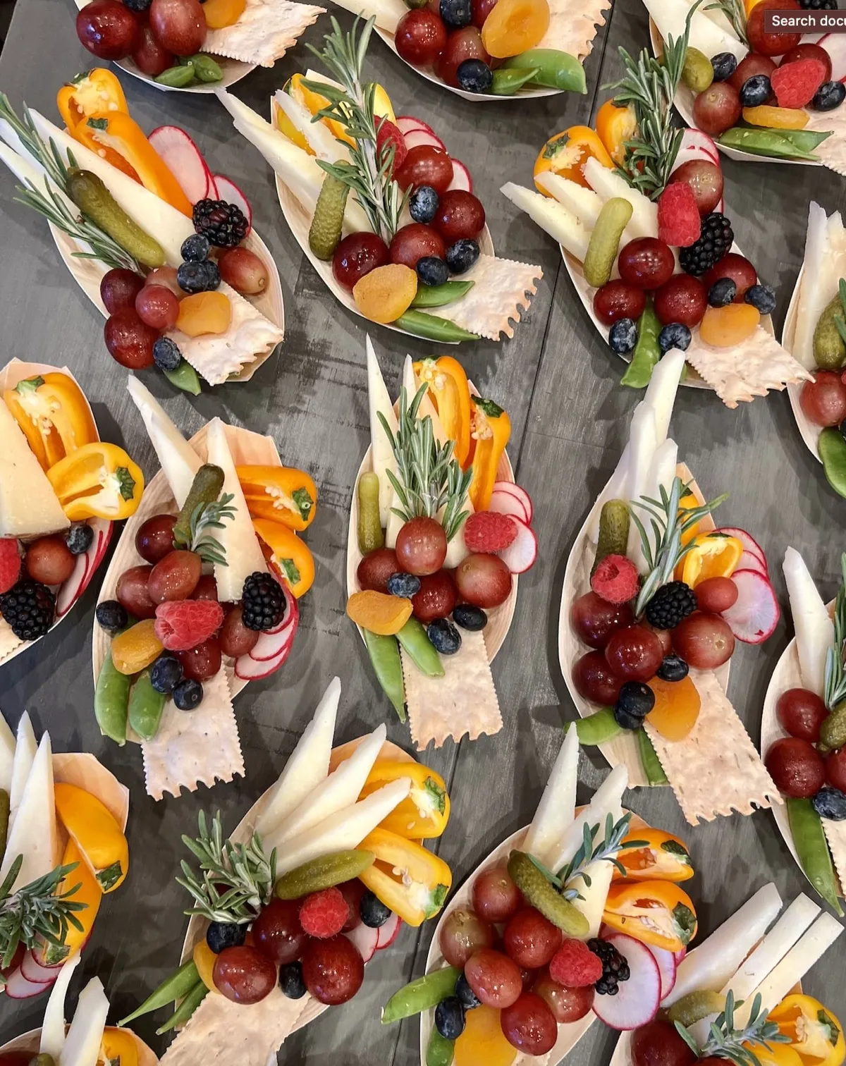 Rows of single-serve charcuterie boats with fruit, cheese and herbs