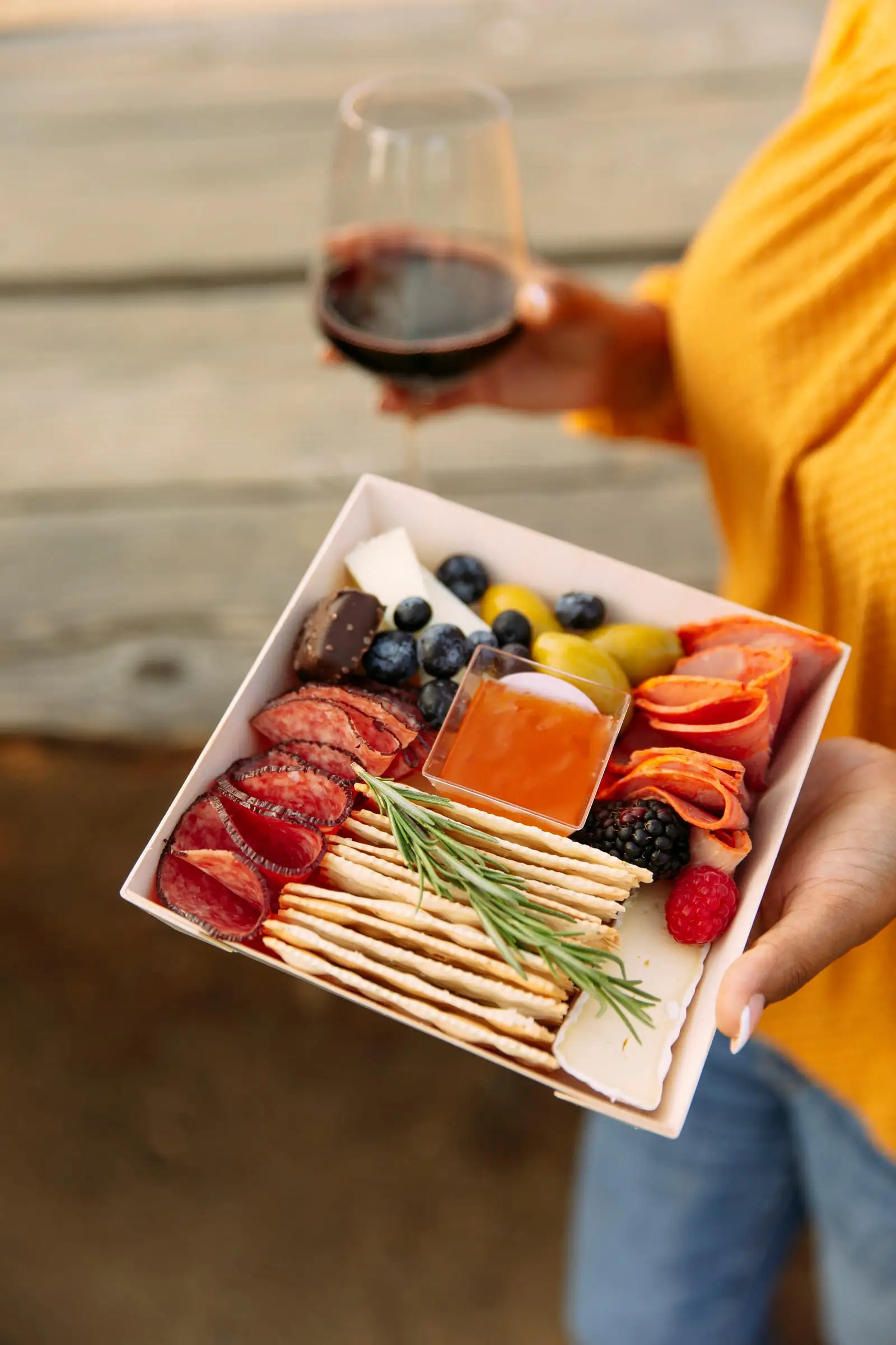 A guest holding a charcuterie box and a glass of wine