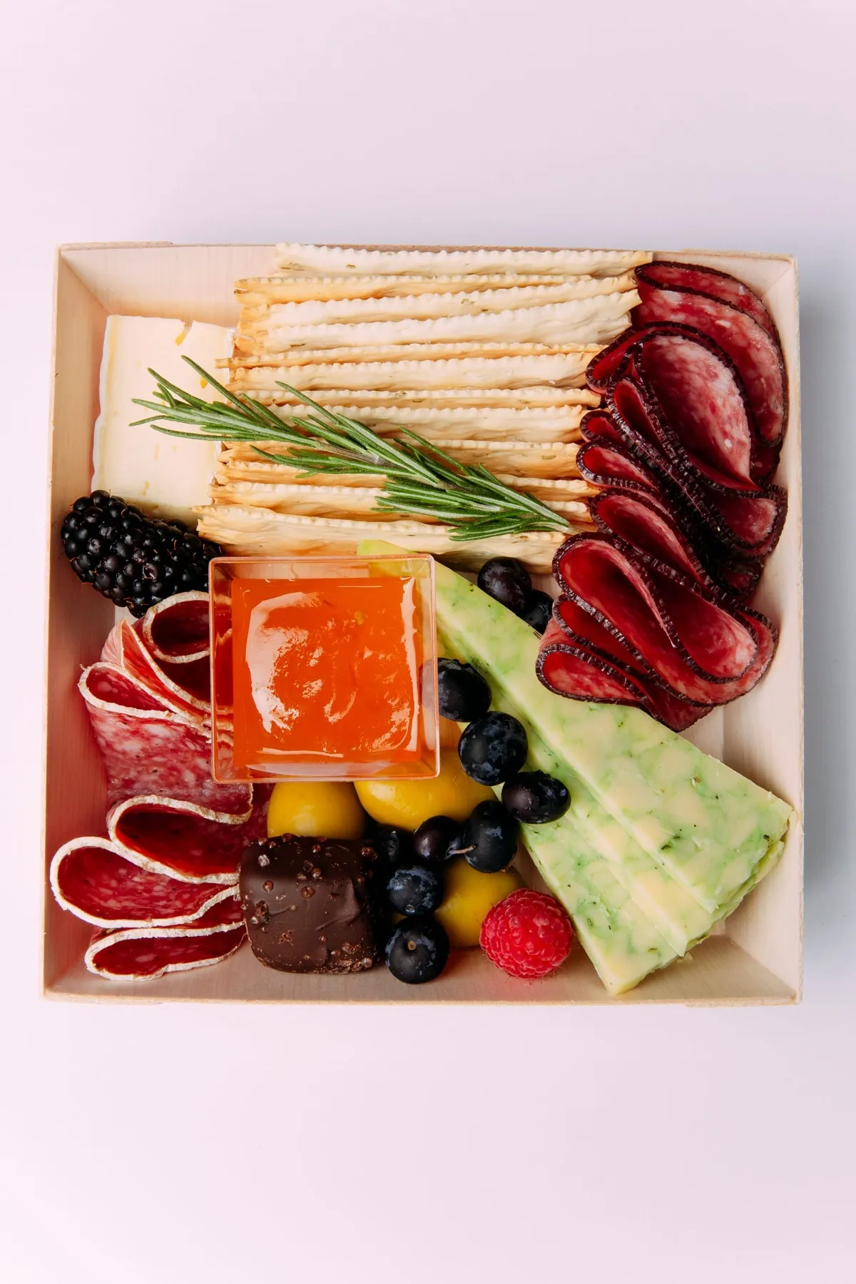 A charcuterie box with jelly, crackers and cured meats