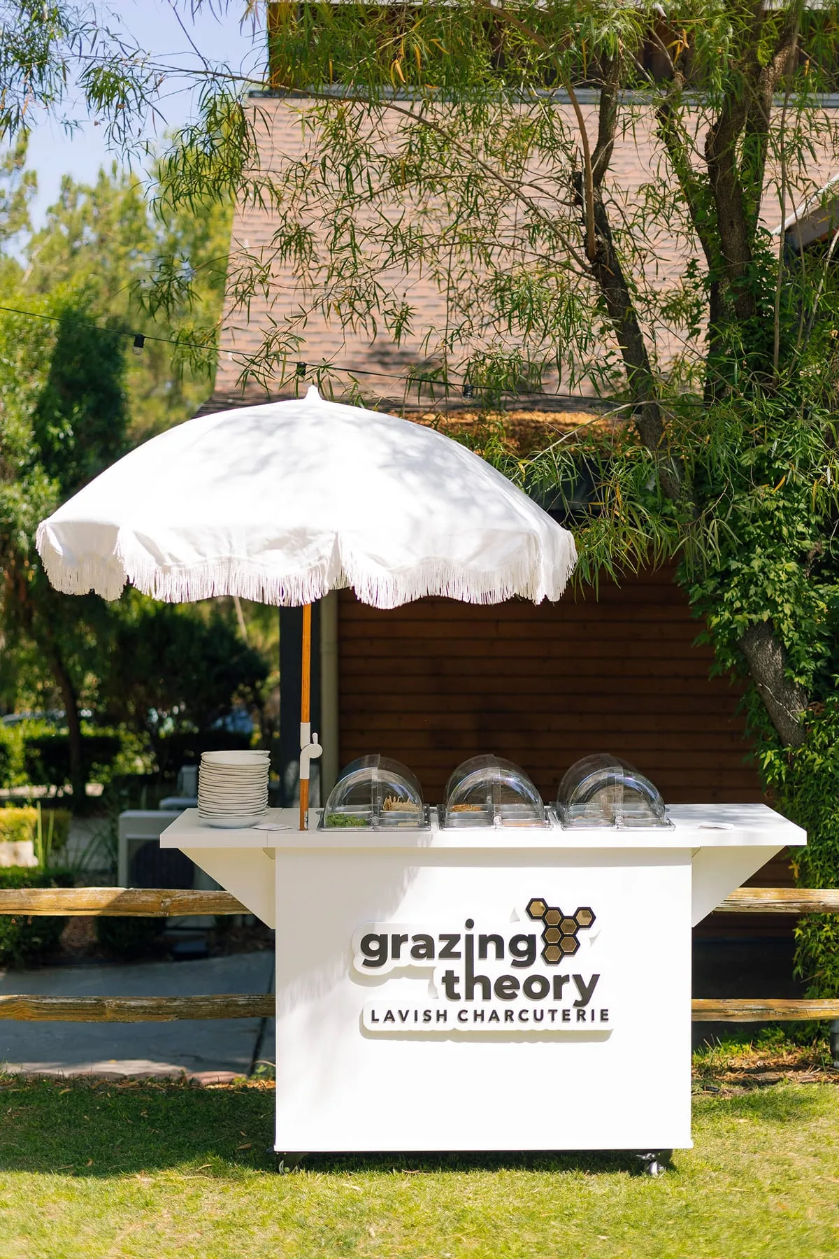 The Grazing Theory charcuterie cart under a white umbrella at a garden wedding