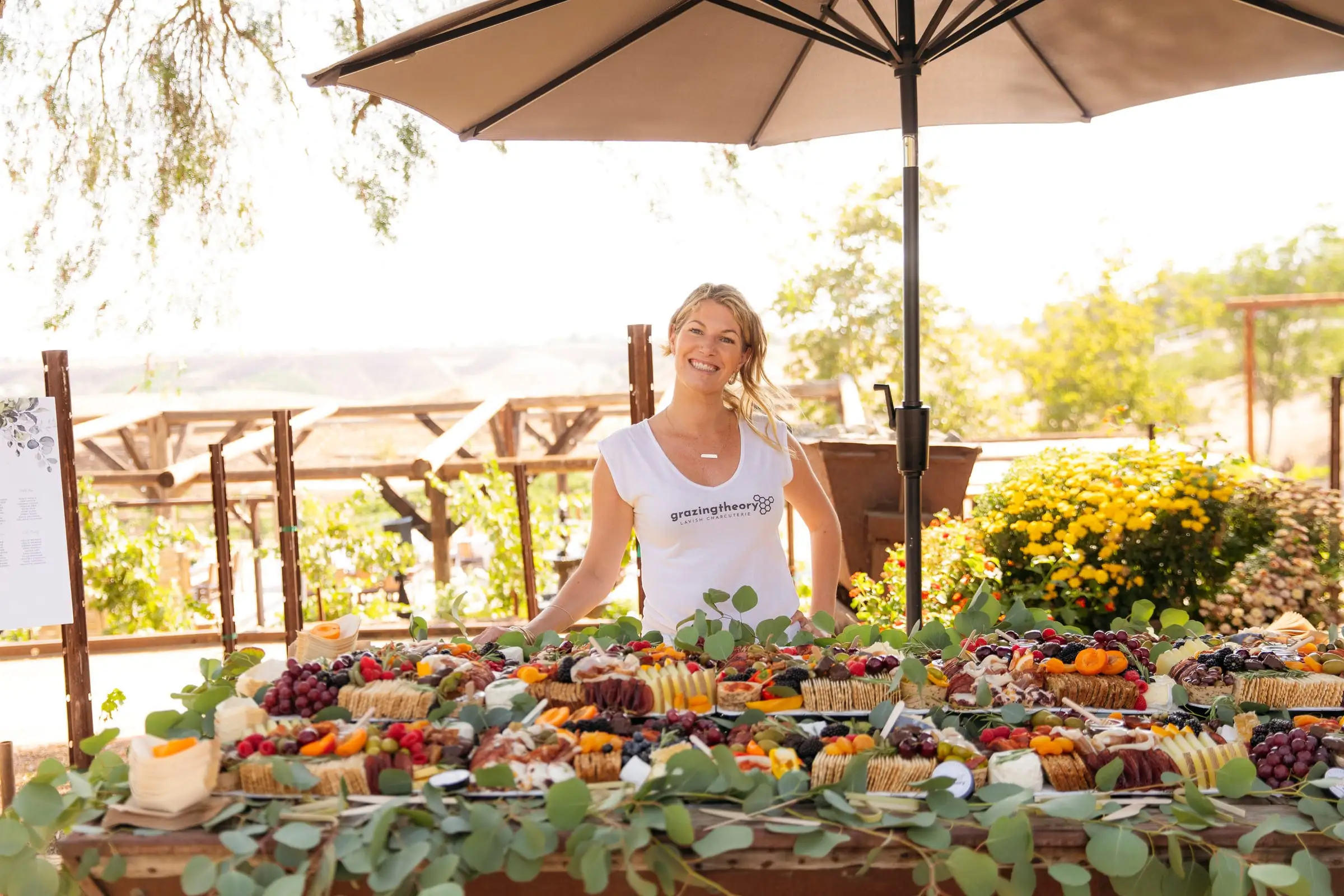 Gina LaMora standing behind a long grazing table of cheeses, cured meats and fruit at a Temecula winery