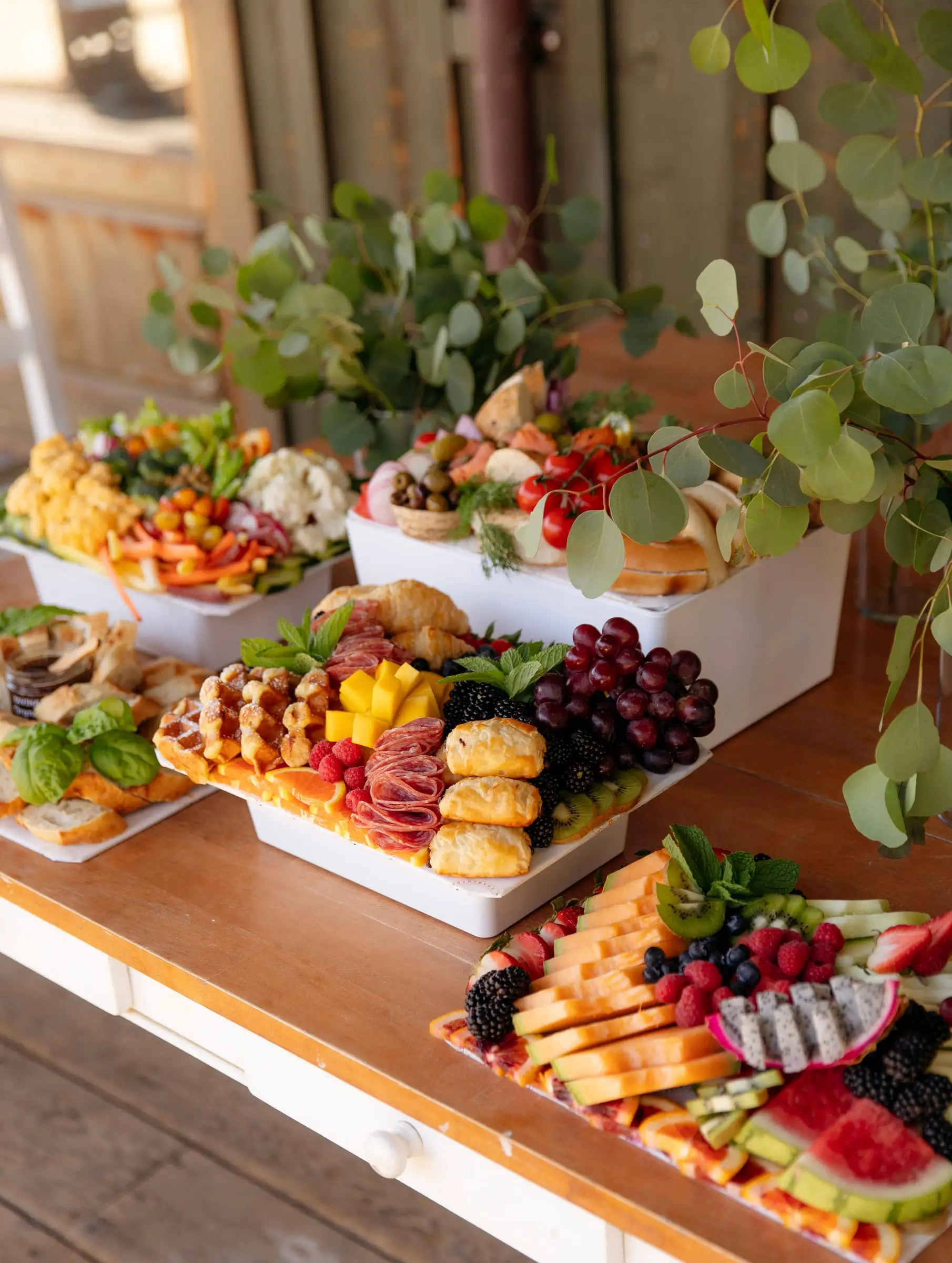 Grazing boards on white risers with greenery at an event