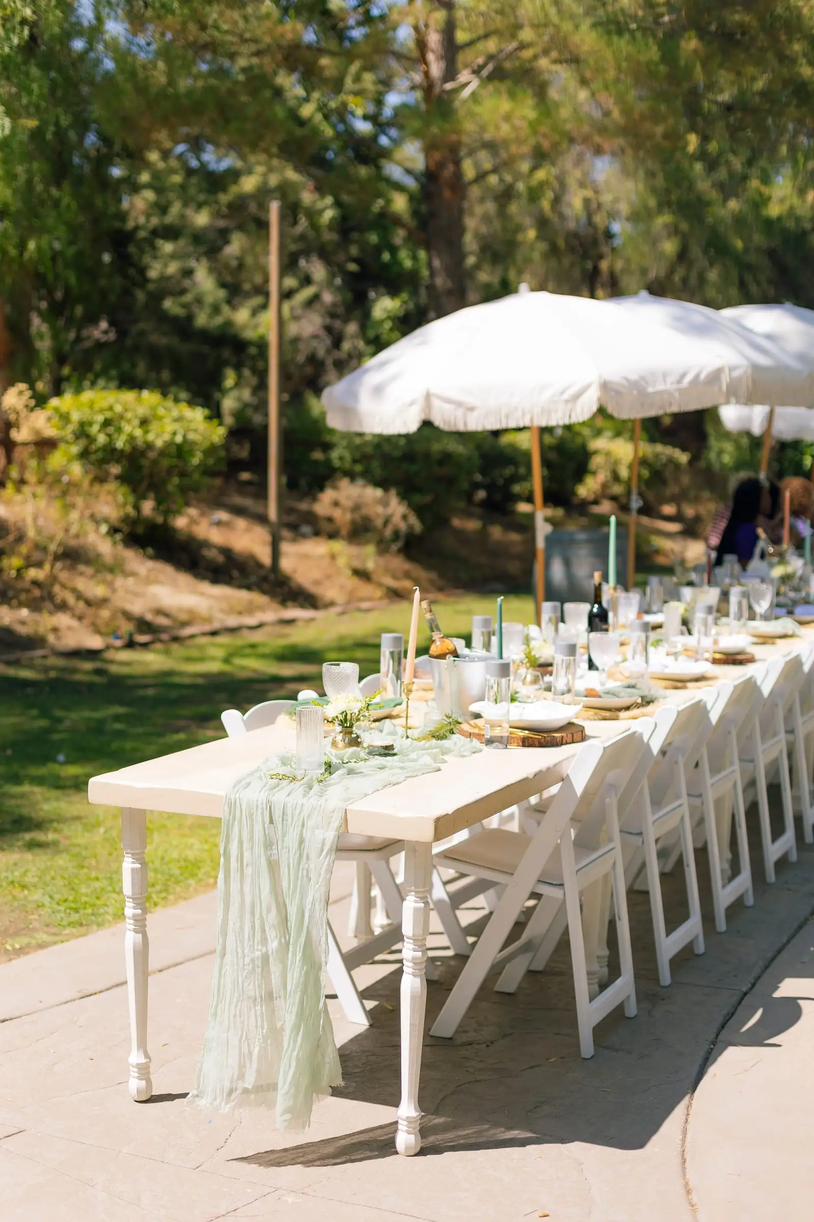 Long outdoor party tables with white umbrellas on a lawn