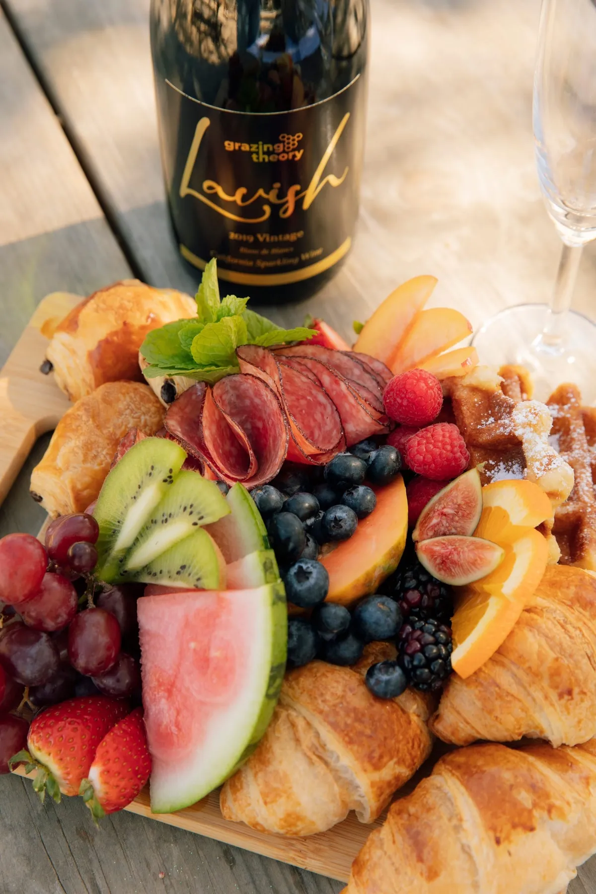 A board with watermelon, cured meats, berries, figs and croissants