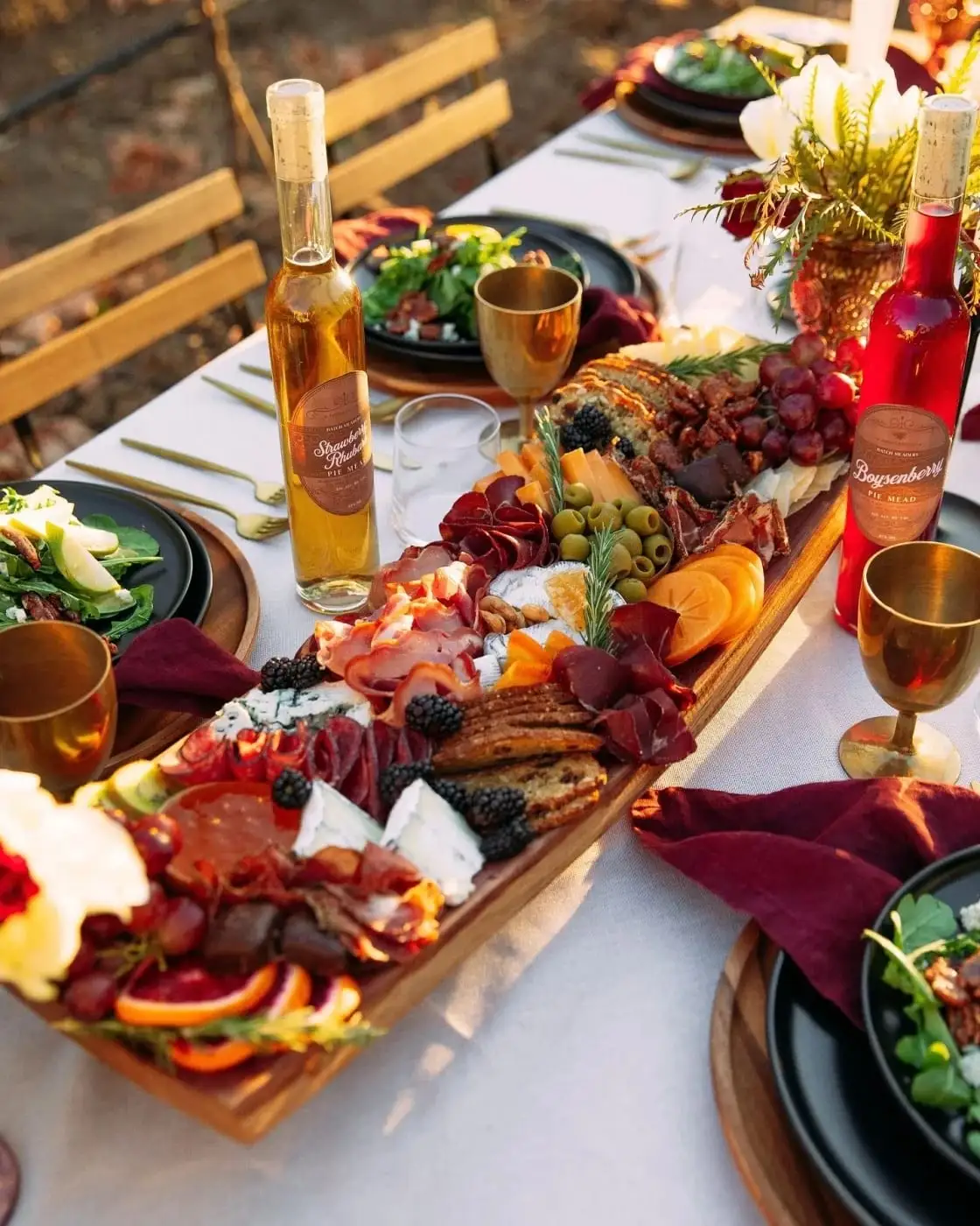 Rehearsal dinner table set with long charcuterie boards, glasses of wine and burgundy napkins
