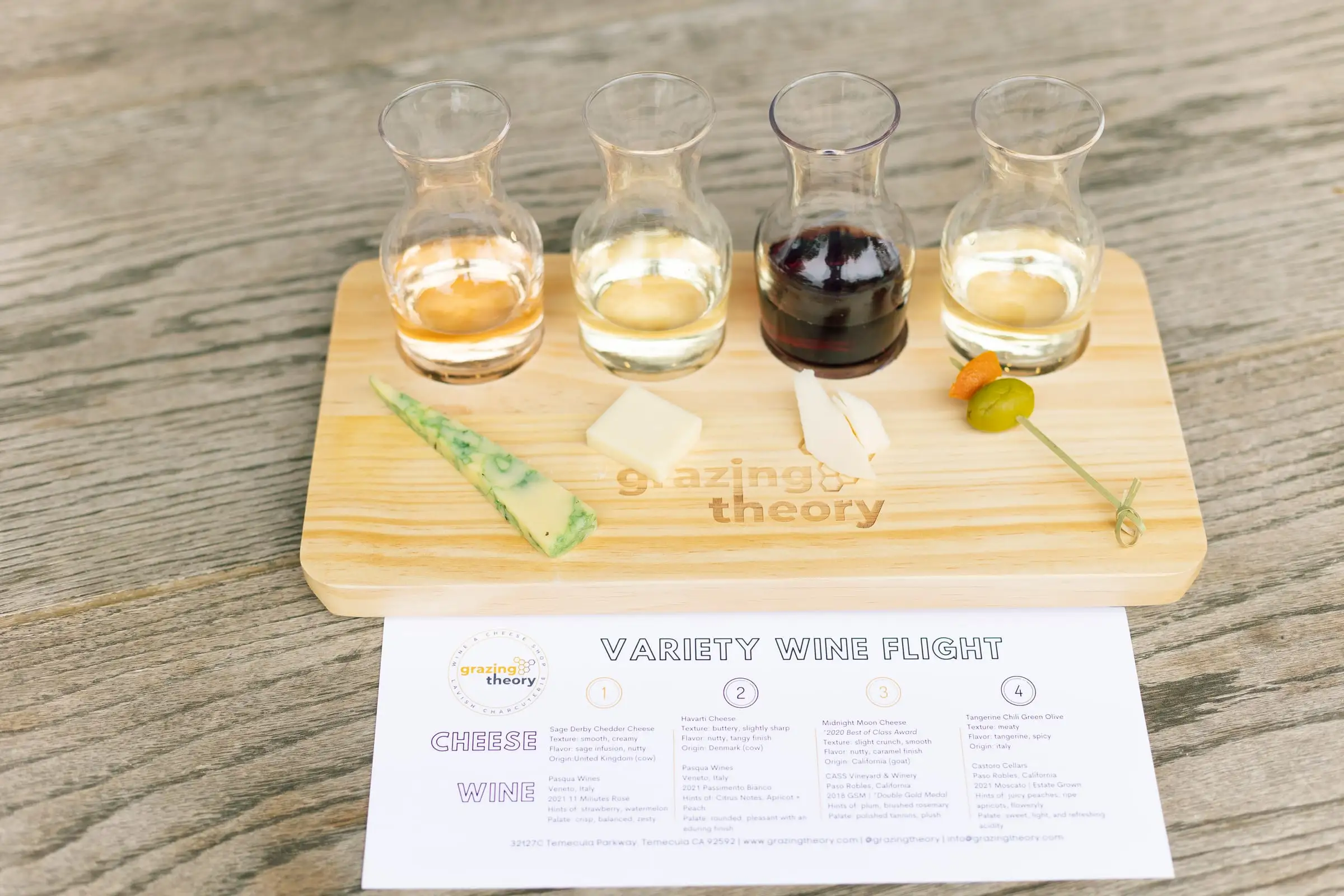 A wine flight of four glasses with a cheese paired to each on a Grazing Theory board