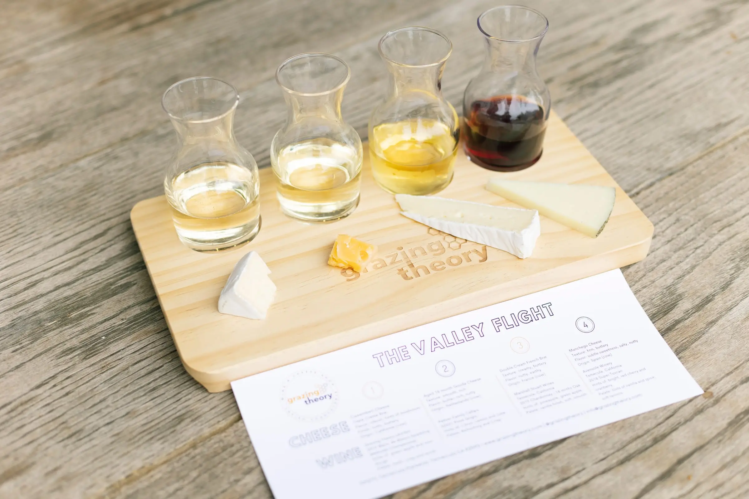 A wine flight with cheeses on a Grazing Theory board